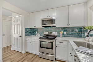 Kitchen with appliances with stainless steel finishes, white cabinets, backsplash, and light stone countertops