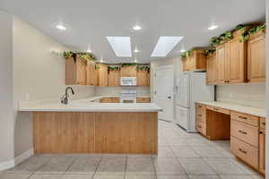 Kitchen with a skylight, light countertops, white appliances, a peninsula, and recessed lighting