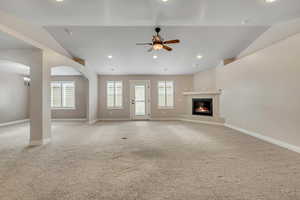 Unfurnished living room featuring carpet flooring, recessed lighting, a fireplace, vaulted ceiling, and arched walkways