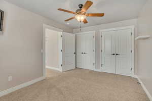 Unfurnished bedroom with multiple closets, light carpet, and ceiling fan