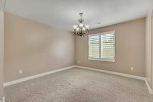 Carpeted empty room featuring a chandelier and baseboards