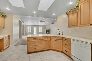 Kitchen featuring light brown cabinetry, dishwasher, light countertops, a glass covered fireplace, and recessed lighting