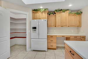 Kitchen featuring light brown cabinets, white refrigerator with ice dispenser, light tile patterned flooring, built in desk, and light countertops