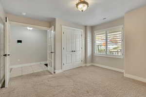 Unfurnished bedroom with light carpet, a closet, light tile patterned floors, and french doors
