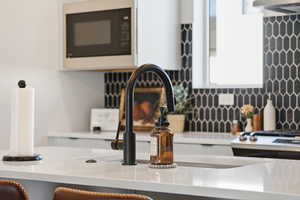Kitchen view of black microwave, light stone countertops, backsplash, and white cabinetry