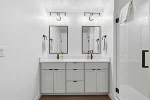 Bathroom featuring double vanity, dark wood-style floors, and a shower stall