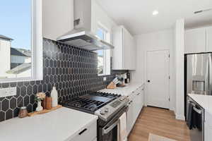 Kitchen with white cabinets, decorative backsplash, range hood, and recessed lighting