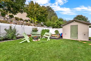 Fenced backyard with a storage shed, a fire pit, and a vegetable garden