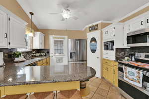 Kitchen featuring backsplash, appliances with stainless steel finishes, hanging light fixtures, light tile patterned flooring, and dark stone counters