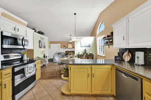 Kitchen featuring decorative backsplash, stainless steel appliances, a peninsula, light tile patterned floors, and lofted ceiling