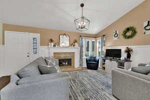 Living room with lofted ceiling, a tile fireplace, a wainscoted wall, and wood finished floors