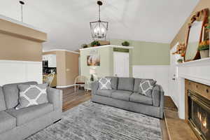 Living room with a glass covered fireplace, a wainscoted wall, vaulted ceiling, wood finished floors, and a chandelier
