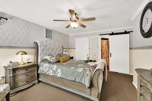 Bedroom featuring a barn door, wallpapered walls, a textured ceiling, a ceiling fan, and crown molding