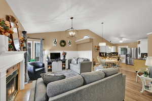 Living area featuring a glass covered fireplace, lofted ceiling, a ceiling fan, light wood finished floors, and a chandelier