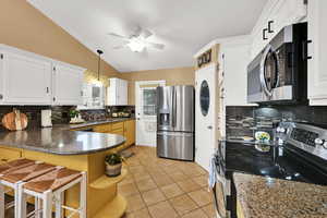 Kitchen with backsplash, stainless steel appliances, light tile patterned flooring, lofted ceiling, and dark stone counters