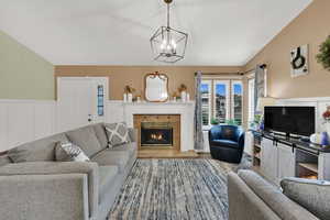 Living room with vaulted ceiling, a fireplace, a wainscoted wall, a chandelier, and wood finished floors