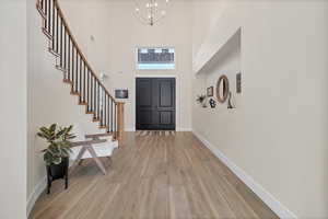 Entryway featuring light wood-style flooring, a towering ceiling, a chandelier, and stairway