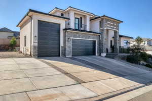 View of front of house with a balcony, stone siding, concrete driveway, and stucco siding