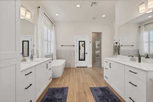 Bathroom with two vanities, tile walls, light wood finished floors, a freestanding tub, and recessed lighting