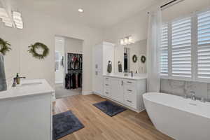 Full bathroom featuring two vanities, a soaking tub, a walk in closet, light wood-type flooring, and recessed lighting
