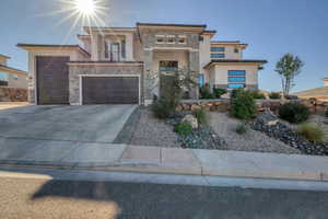 View of front facade with stone siding, a balcony, concrete driveway, and stucco siding