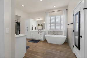 Full bath featuring vanity, tile walls, a freestanding bath, a spacious closet, and light wood-style floors