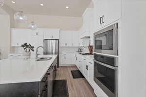 Kitchen featuring appliances with stainless steel finishes, hanging light fixtures, light wood-style floors, white cabinets, and backsplash