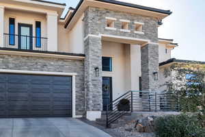 View of front of property featuring stone siding, stucco siding, concrete driveway, a balcony, and a garage