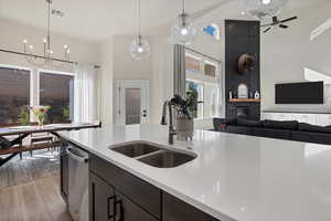Kitchen featuring decorative light fixtures, light wood-type flooring, light stone counters, open floor plan, and a towering ceiling