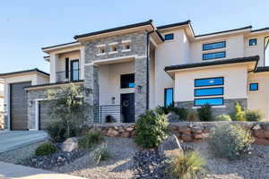 Modern home with stone siding, a balcony, stucco siding, a garage, and concrete driveway