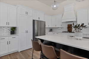 Kitchen featuring backsplash, white cabinets, freestanding refrigerator, light wood-style floors, and pendant lighting