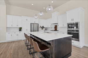 Kitchen with dark brown cabinetry, stainless steel appliances, a spacious island, backsplash, and white cabinets