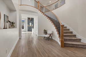 Foyer entrance featuring a high ceiling, stairway, light wood-style floors, and a fireplace