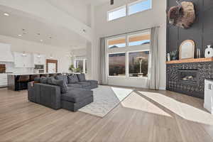 Living room featuring a tile fireplace, a towering ceiling, a chandelier, plenty of natural light, and light wood finished floors