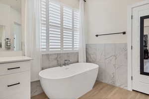 Full bath featuring tile walls, a freestanding tub, light wood-style floors, a wainscoted wall, and vanity
