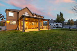 Back of house at dusk featuring a patio area, stucco siding, a yard, a trampoline, and a ceiling fan