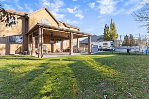 Back of house with a trampoline, a ceiling fan, stucco siding, and a lawn