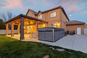 Back of property at dusk featuring a patio area, ceiling fan, stucco siding, and a hot tub