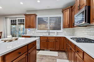 Kitchen featuring light wood finished floors, appliances with stainless steel finishes, brown cabinets, light stone countertops, and recessed lighting