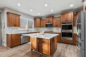 Kitchen with brown cabinetry, stainless steel appliances, decorative backsplash, recessed lighting, and light wood-style flooring