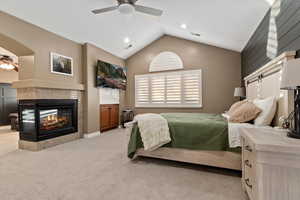 Bedroom featuring lofted ceiling, carpet flooring, a ceiling fan, and a tiled fireplace