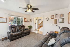 Carpeted living room with ceiling fan and stairway