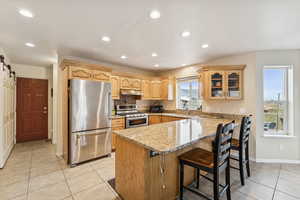 Kitchen featuring appliances with stainless steel finishes, a breakfast bar area, light stone countertops, glass insert cabinets, and light tile patterned flooring