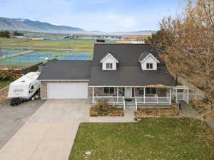 Cape cod-style house with covered porch, a mountain view, a front yard, driveway, and a garage