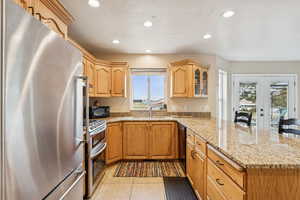 Kitchen with appliances with stainless steel finishes, french doors, light stone countertops, recessed lighting, and a peninsula