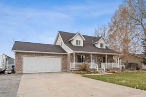 Cape cod-style house with covered porch, driveway, a shingled roof, a garage, and a front lawn