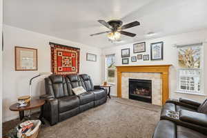Carpeted living room with a tiled fireplace and ceiling fan