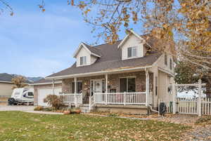 Cape cod-style house with covered porch, a shingled roof, brick siding, a gate, and a garage