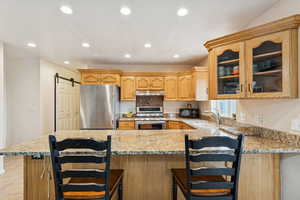 Kitchen featuring appliances with stainless steel finishes, light stone countertops, a barn door, a breakfast bar area, and recessed lighting