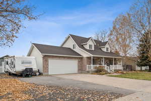 View of front of home with a porch, roof with shingles, driveway, brick siding, and an attached garage